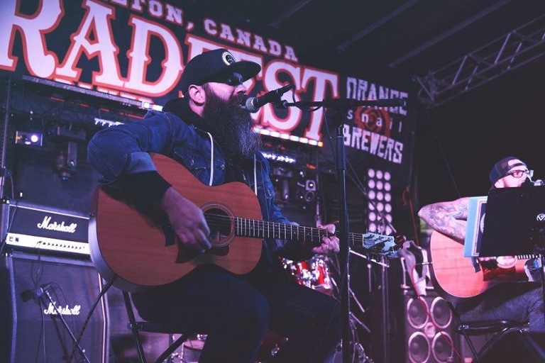 Musician playing an acoustic guitar and singing on stage at Radfest in Milton.